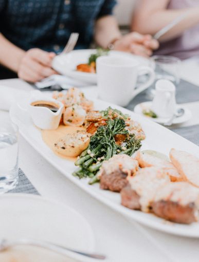 Meat on white plate with couple eating in background